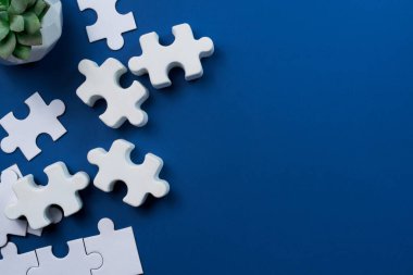 Beyaz yapboz parçaları küçük bir bitkinin yakınındaki derin mavi bir zemine saçılmış. Boşluğu Kopyala