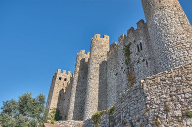 Obidos 'un duvarları, silindirik kuleler ve bitki örtüsüyle kaplı bir arazinin üzerindeki mazgallarla yükseliyor. Ortaçağ karakterlerini vurgulayan düzensiz taşlarla inşa edilmiş.. 