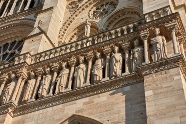 Paris 'teki Notre Dame cephesinin yakın çekimleri dini figürler, krallar ve azizlerin taç, cübbe ve sembolik objelerle resmedildiği yontulmuş taş heykeller ortaya çıkardı. Gotik kemerler ve tepe noktalarıyla çerçevelenen bu ortaçağ eserleri, ciddiyeti ifade ediyor.