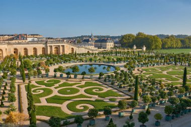 Versailles Sarayı 'nın bahçesindeki Parterre de Orangerie' ye yolların simetrik bileşimi, saksılarda ağaçlar ve merkezde dairesel bir gölet sunulur. Klasik taş mimarisi ve anıtsal kemerler manzarayı çerçeveliyor