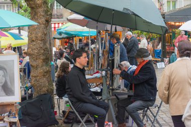 Paris, Fransa - 14 Ekim 2025, In Place du Tertre, Montmartre 'ın sanatsal kalbi, turistler, şövaleler ve gülümseyen mankenlerle çevrili birçok ressam açık havada çalışır. Atmosfer dinamik ve yaratıcı, sıcak renklerle.