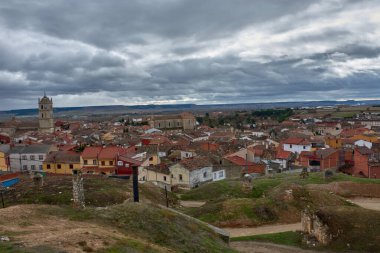 Palencia vilayetindeki Duenas 'ın panoramik manzarası, köyün kırmızı çatılı evleri ve Santa Maria de la Asuncion Kilisesi' nin dramatik, bulutlu gökyüzüne karşı ayakta duran kulesiyle birlikte yemyeşil bir tepeden gözler önüne seriliyor.. 