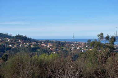 San Andres de Comesana tepelerinden görülen Ria de Vigo 'nun yüksek manzarası, konut binaları, canlı bir haliç ve açık bir gökyüzü içerir. Görüntü, kentsel gelişim ve doğa arasındaki uyumu yakalıyor ve sahil şeridini gösteriyor.