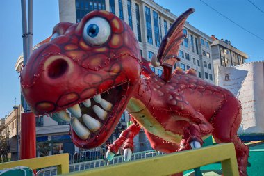 A large red dragon with a friendly expression is the star of this float, distinguished by its detailed scales and perimeter lighting of small bulbs. The figure is surrounded by fairytale elements, such as a giant book