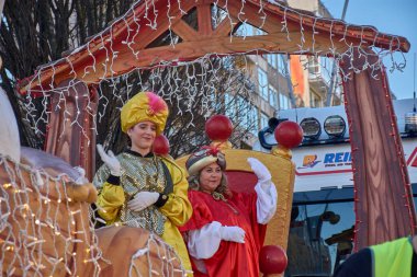 Vigo, Pontevedra, İspanya, 5 Ocak 2026, görkemli kırmızı kadife ve parıldayan altın kumaşlarla süslenmiş iki kraliyet sayfası, beyaz ışık çelenkleriyle süslenmiş şamandıralarından kalabalığı coşkuyla selamlıyor..