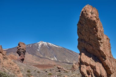 Roque Cinchado 'nun heybetli dikey yapısı ön plana hakim olurken Teide Dağı' nın görkemli karlı zirvesi ihtişamlı bir şekilde yükseliyor..