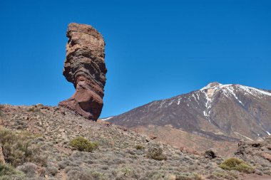 Roque Cinchado 'nun heybetli dikey yapısı ön plana hakim olurken Teide Dağı' nın görkemli karlı zirvesi ihtişamlı bir şekilde yükseliyor..