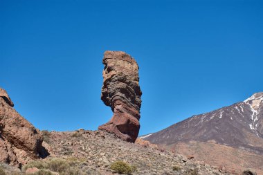 Roque Cinchado 'nun heybetli dikey yapısı ön plana hakim olurken Teide Dağı' nın görkemli karlı zirvesi ihtişamlı bir şekilde yükseliyor..