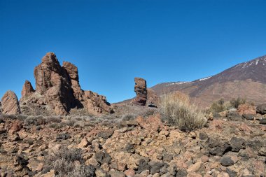 İspanya 'nın Tenerife Ulusal Parkı' ndaki Roque Cinchado 'nun heybetli dikey yapısı. Bazalt kayanın koyu renkleri, zirvenin beyazı ve Kanarya Adası gökyüzünün yoğun maviliği arasındaki çarpıcı tezat.