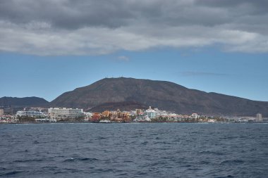 Tenerife 'deki Adeje sahili, evleri ve otelleri palmiye ağaçlarıyla çevrili sahil şeridi ile okyanus tarafından turlanan volkanik kumsallara yol açıyor. Adanın güneyindeki sıcak ışık denizin maviliği arasındaki zıtlıkları vurgular.