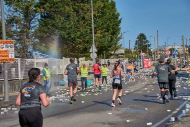 Nigran, Pontevedra, İspanya; 6 Nisan 2025: Yüksek görüşlü yelek giyen genç gönüllüler İspanya 'nın Nigran kentinde düzenlenen Vig Bay Half Marathon sırasında koşuculara suya batırılmış sünger dağıtıyorlar. Sahne, toplum desteği ve ekip çalışmasının bir anını partik olarak yakalıyor.