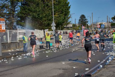 Nigran, Pontevedra, İspanya; 6 Nisan 2025: Yüksek görüşlü yelek giyen genç gönüllüler İspanya 'nın Nigran kentinde düzenlenen Vig Bay Half Marathon sırasında koşuculara suya batırılmış sünger dağıtıyorlar. Sahne, toplum desteği ve ekip çalışmasının bir anını partik olarak yakalıyor.