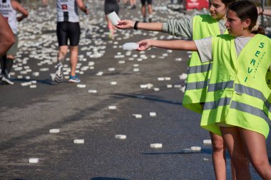 Nigran, Pontevedra, İspanya; 6 Nisan 2025: Yüksek görüşlü yelek giyen genç gönüllüler İspanya 'nın Nigran kentinde düzenlenen Vig Bay Half Marathon sırasında koşuculara suya batırılmış sünger dağıtıyorlar. Sahne, toplum desteği ve ekip çalışmasının bir anını partik olarak yakalıyor.