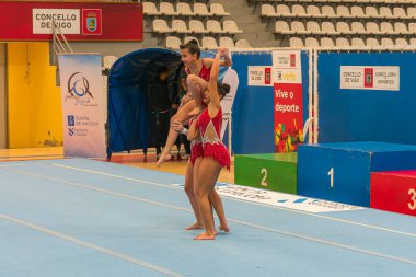 Vigo, İspanya, 21 Şubat 2026, Vigo 'da düzenlenen uluslararası jimnastik şampiyonası sırasında genç bayan sporcular açık mavi bir minder üzerinde etkileyici bir denge ve güç gösterisi yapıyorlar. Bu dinamik kompozisyon, görsel olarak h