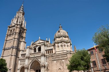 Toledo Katedrali Ayuntamiento Meydanı 'ndan alınan parlak mavi gökyüzünün altında görkemli bir şekilde duruyor. Sıcak taş tonlar, gotik kubbe ve barok kubbe görsel olarak zengin ve tarihsel açıdan önemli bir kompozisyon oluşturur.