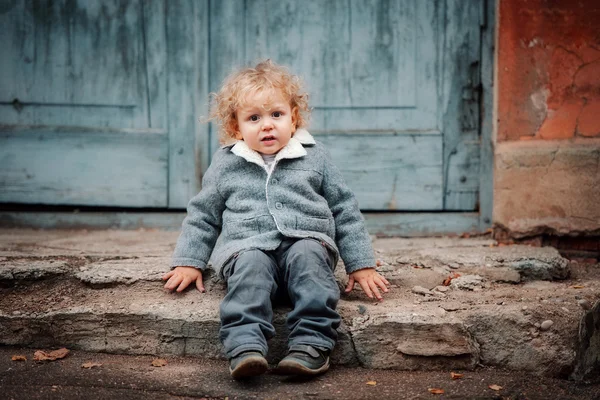 Маленький мальчик сидит у деревянных дверей — стоковое фото