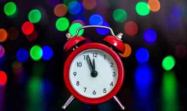 Renkli ışıkların arka planına karşı elleri olan saat gece yarısına beş dakika var. Bokeh. Yeni Yıl.