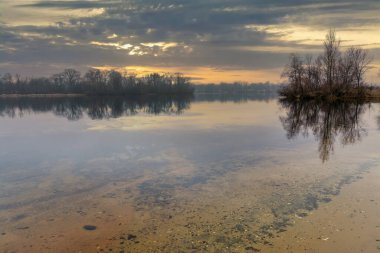 Rezervuarın orada şafak vakti. Nehir boyunca uzanan orman suya yansıyor. Sakin doğa sahnesi.