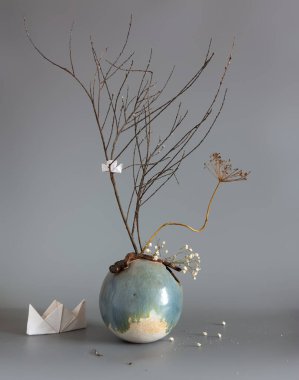 Yuvarlak bir vazoda kurumuş bitkiler ve kağıt tekneler kompozisyonu.