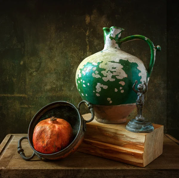 Still life with a ripe pomegranate in a copper dish, a peeling ceramic jug and a very old cast iron figurine. Retro. Vintage.