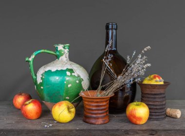 Çok eski bir seramik sürahi, soyulmuş boya, büyük koyu kahverengi bir şişe, bir demet lavanta ve olgun elmalarla seramik bir vazo. Eski model. Durgun hayat