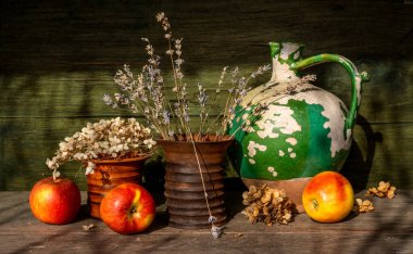 Çok eski bir seramik sürahi, soyulmuş boya, iki seramik vazo kurutulmuş çiçek, ve olgun elmalar. Eski.