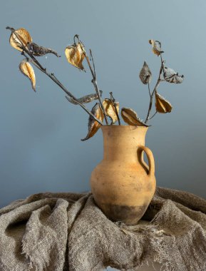 Çuval bezle kaplı bir masanın üzerinde kurumuş dalları olan eski bir seramik sürahi. Eski model. Retro.