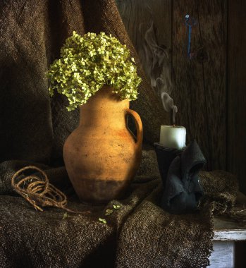 Çuval bezinin üzerinde kurumuş ortanca olan eski bir seramik sürahi ve keşiş şeklinde bir şamdanda söndürülmüş bir mum. Eski model. Retro.