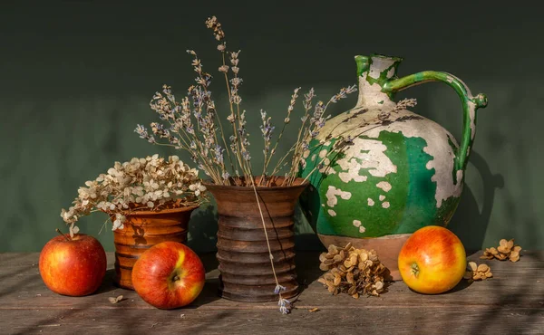 一个非常古老的陶瓷壶 有剥皮的油漆 两个陶瓷花瓶的干花 和成熟的苹果 — 图库照片