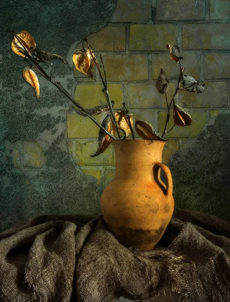 Çuval bezle kaplı bir masanın üzerinde kurumuş dalları olan eski bir seramik sürahi. Eski model. Retro.