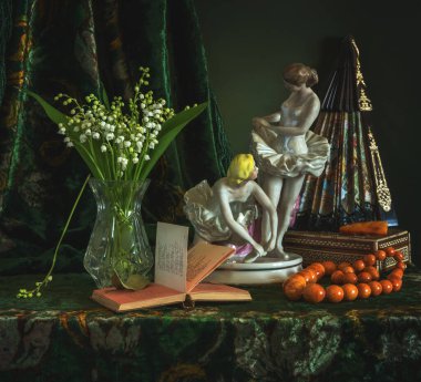 Eski porselen balerin figürleri. Açık kitap. Bir buket mis kokulu zambak ve kehribar boncuklar..