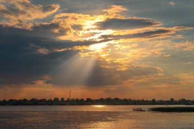 Nehirde gün batımı. Güneş ışınları bulutların arasından yol alır. Hava güzel..