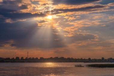 Nehirde gün batımı. Güneş ışınları bulutların arasından yol alır. Hava güzel..