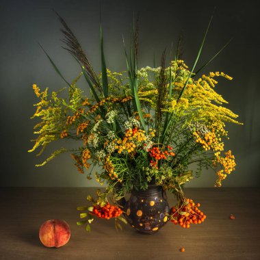 Bir buket çayır çiçeği ve kırmızı böğürtlenli rowan dalları. Masada olgun şeftali.