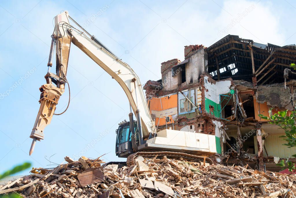 An excavator demolishes a brick house. Renovation concept of old dilapidated housing.