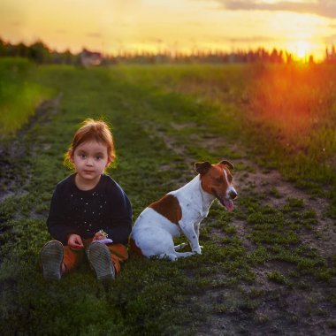 Doğada köpeği olan bir çocuk. Gün batımında yeşil çimlerde oynayan bir kız.