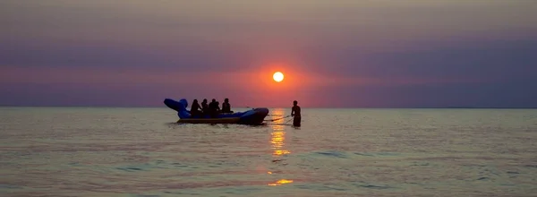 Группа туристов на надувном банане на закате... надувная лодка в форме банана на закате. Веселье и хорошие воспоминания в море на закате. панорамная фотография — стоковое фото
