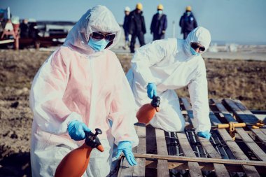 Takım elbiseli, eldivenli, maskeli bir çalışan yüzey dezenfekte eder.