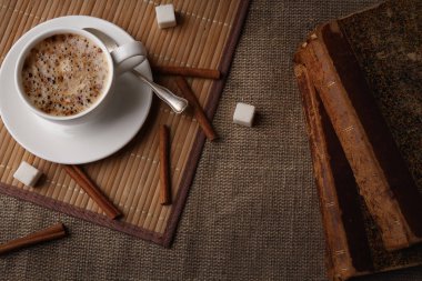 Çuval bezinin üzerinde beyaz kahve, tarçın, şeker ve antika kitaplar.