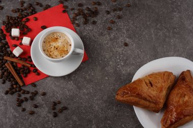 Masanın granit dokusunda beyaz bir fincan kahve, tarçın, şeker ve pasta.