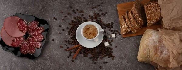 Panorama with a cup of coffee, beans, bread and sausage on the granite texture of the table
