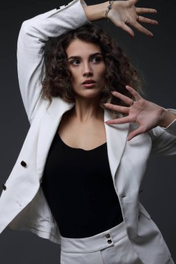 Beyaz takım elbiseli, gri arka planda güzel bir kızın stüdyo portresi.