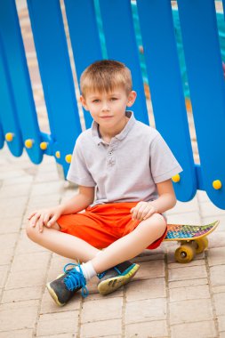 Bir kaykay üzerinde arka plan mavi çit oturan çocuk