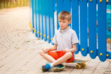 Oğlan mavi çit yakınındaki bir kaykay üzerinde oturan üzgün