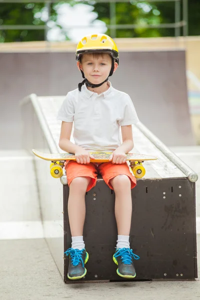 Garçon en chapeau assis avec une planche à roulettes et un sourire sur son visage — Photo