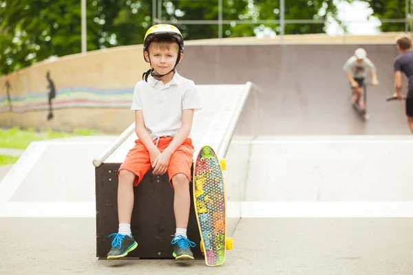 Garçon en chapeau assis avec une planche à roulettes et un sourire sur son visage — Photo