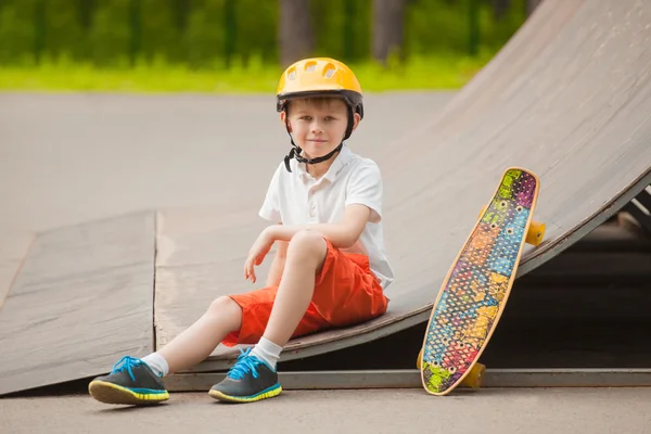 Garçon en chapeau assis à côté d'un skateboard et souriant — Photo