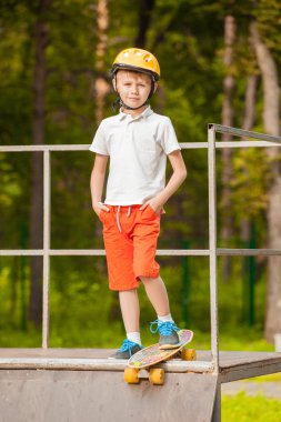 Bir kaykay üzerinde duran ve gülümseyen şapkalı çocuk