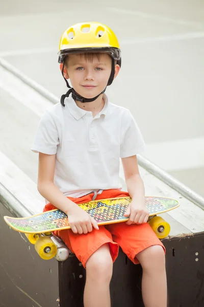 Garçon en chapeau assis avec une planche à roulettes et un sourire sur son visage — Photo