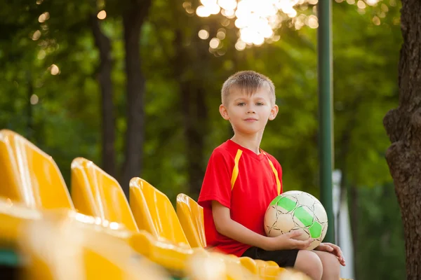 Chlapec s míčem na lavičce fanoušků — Stock fotografie